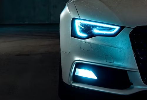 A close-up view of the front passenger-side headlight and bumper of a silver car, illuminated with bright blue LED lights.