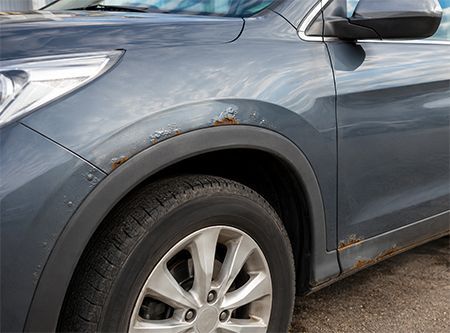 Blue SUV with rust and scratches on the front fender and side panel