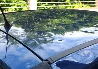 A blue car roof covered in numerous round dents caused by a recent hailstorm.