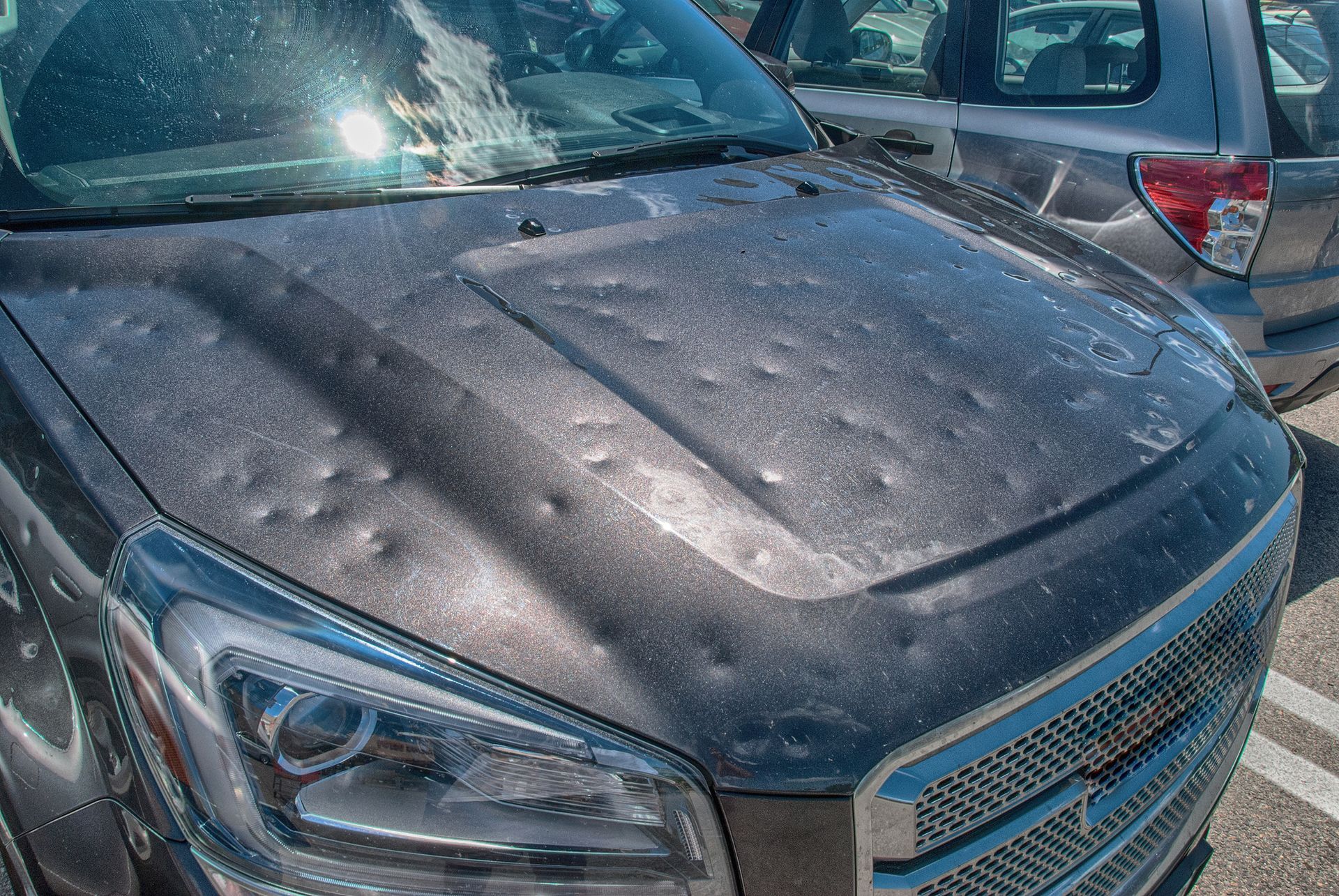 Dust-covered black SUV parked close to another vehicle, front hood and windshield visible