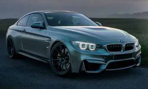 A silver BMW M4 coupe parked on an asphalt road at twilight.