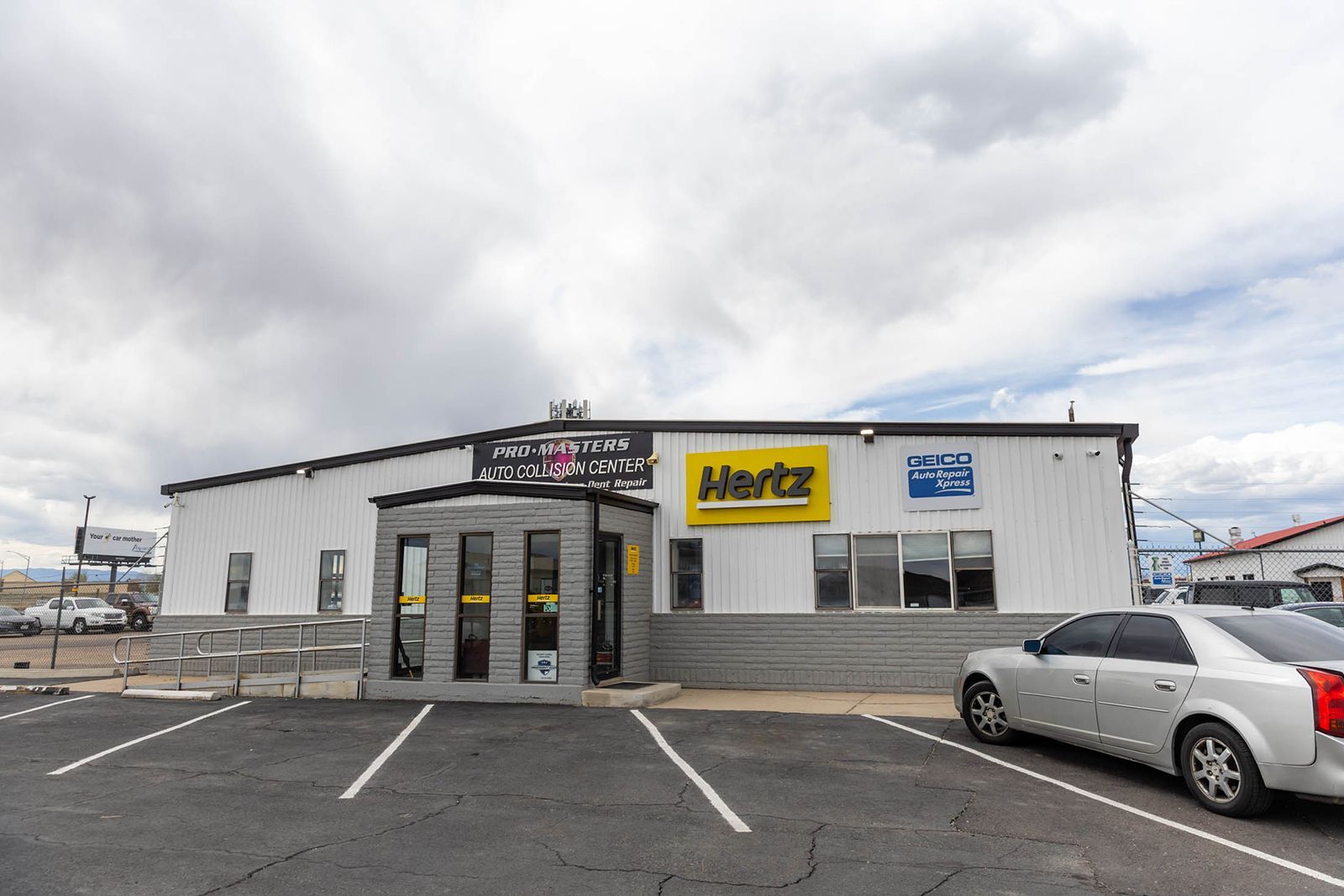 Small commercial building with signs, a silver car parked outside, and an overcast sky.