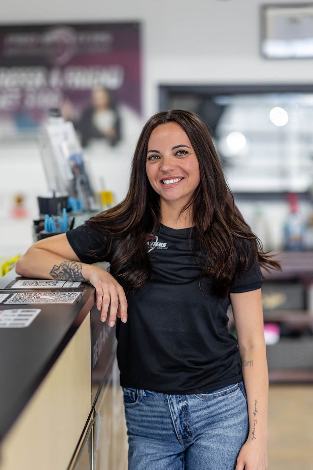 Smiling woman in a black shirt and jeans leaning on a counter in a store