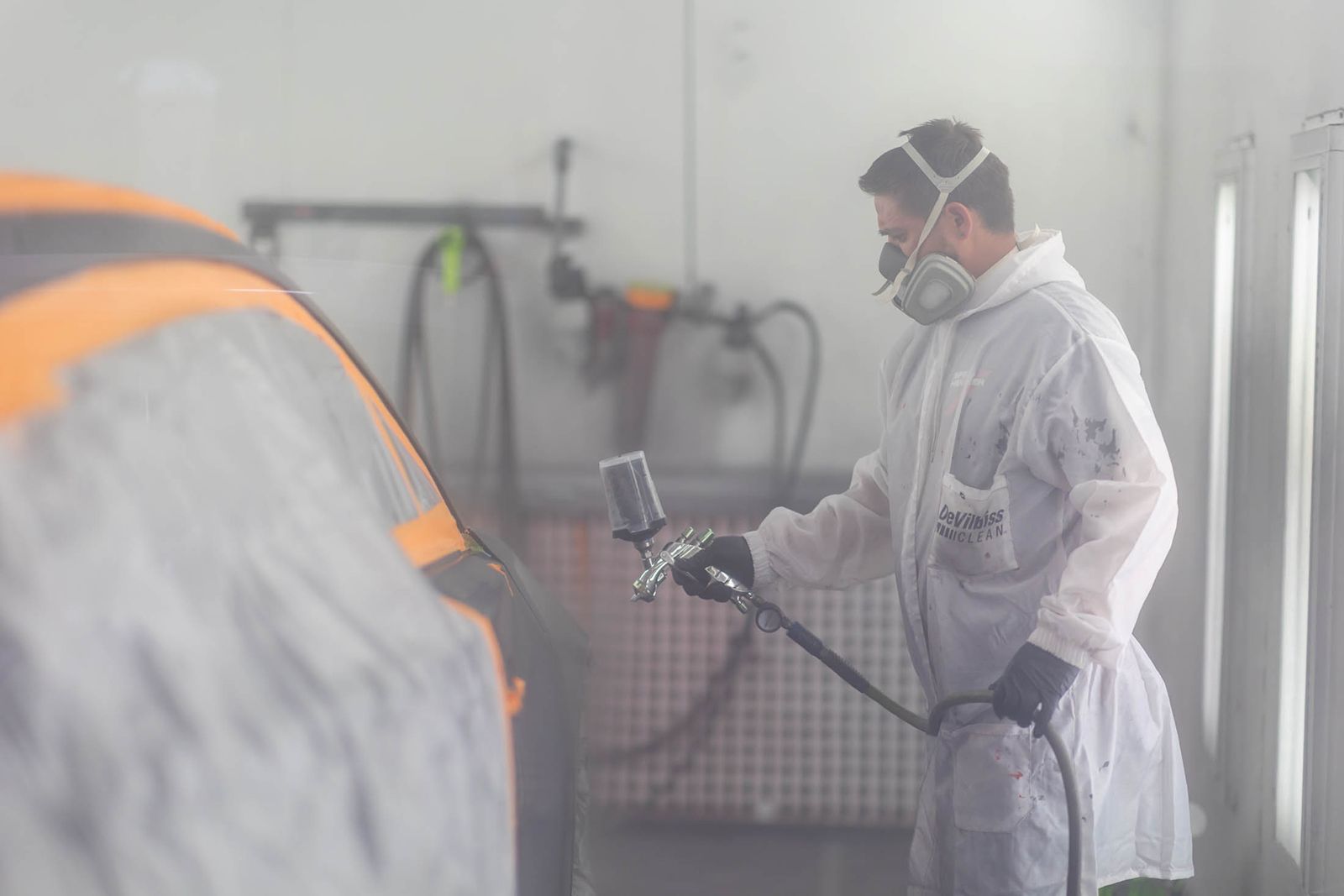 Worker in protective suit spray-painting a surface in a hazy paint booth