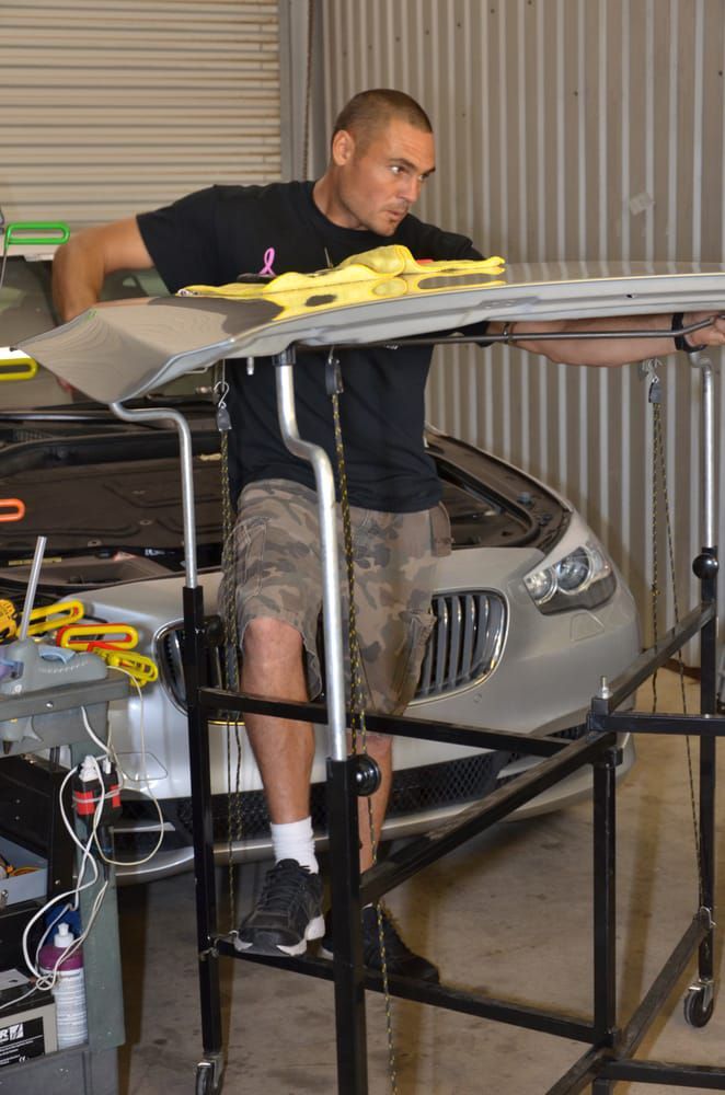 Man working on a model car indoors, leaning over a metal workbench with tools nearby