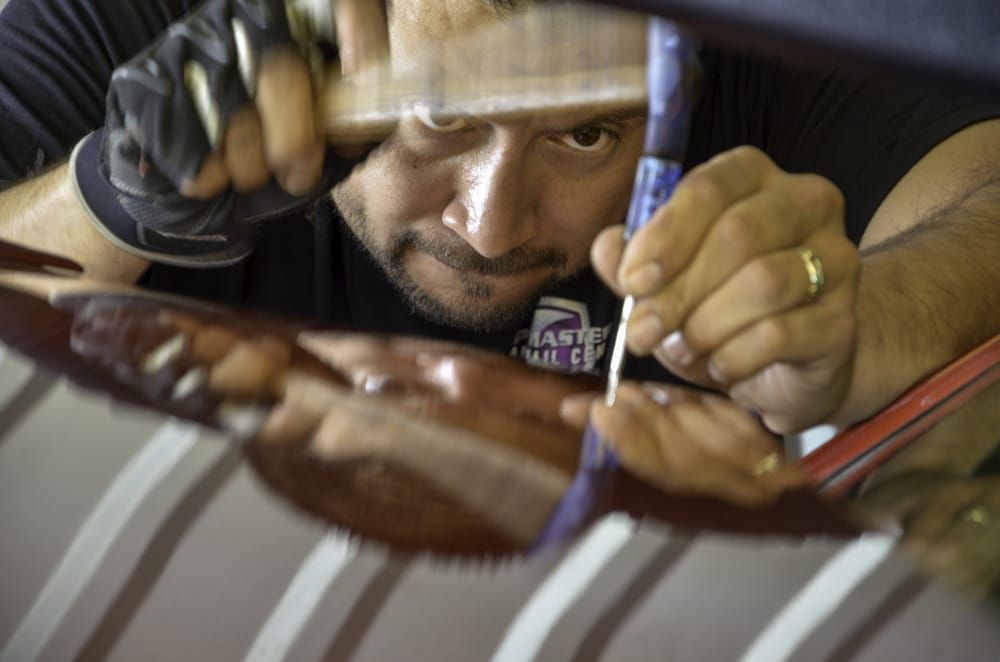 Worker crouched over a glossy brown surface, carefully applying tool marks with gloves on.