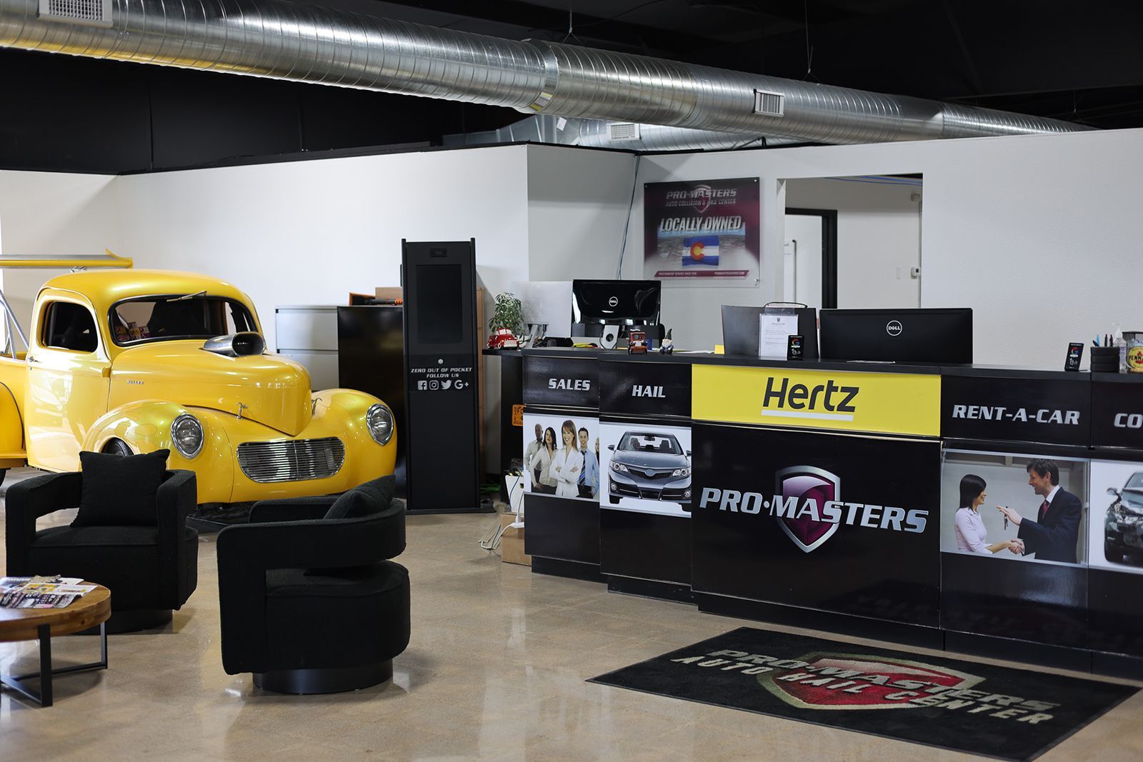 Yellow vintage car displayed in a showroom beside Hertz and RaceMasters promotional counters