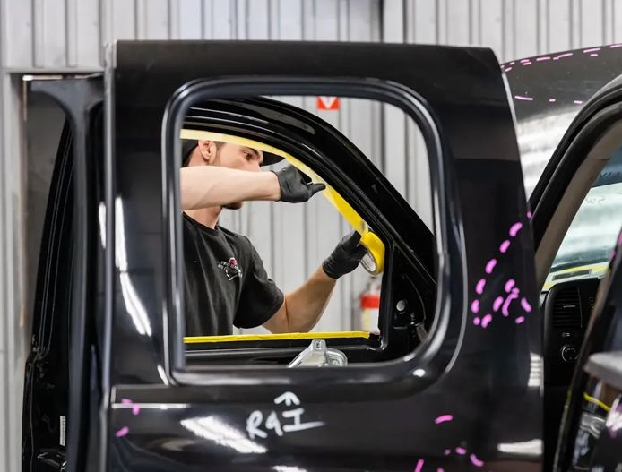 Person working inside a black vehicle at an auto shop, visible through the open side window.