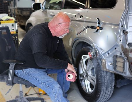 Man in respirator spray-painting a black car panel in a workshop.