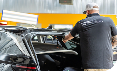 Worker loading luggage into a black SUV at an indoor car service area