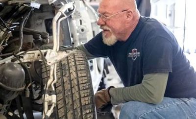 Man inspecting a car tire in a garage, wearing glasses and a dark t-shirt.