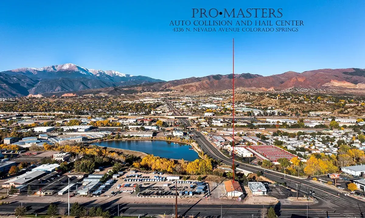 Aerial view of a town with a lake and mountains in the background under a blue sky, autumn colors.