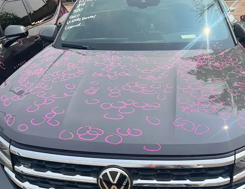 Gray SUV hood with pink circle markings, likely from hail damage. A Volkswagen logo is visible.