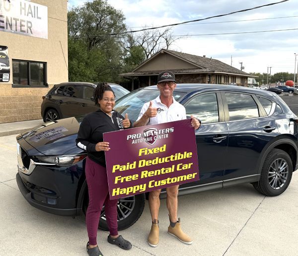 Two people with a blue SUV holding a sign: 