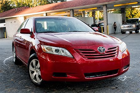 Red Toyota sedan parked outside a car wash with a wet pavement.