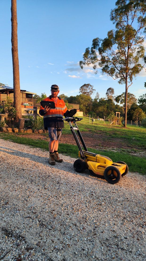 Man Holding Wood, Standing Next to a Yellow Robotic Lawnmower on a Gravel Path — Found It Down Under in Gunalda, QLD