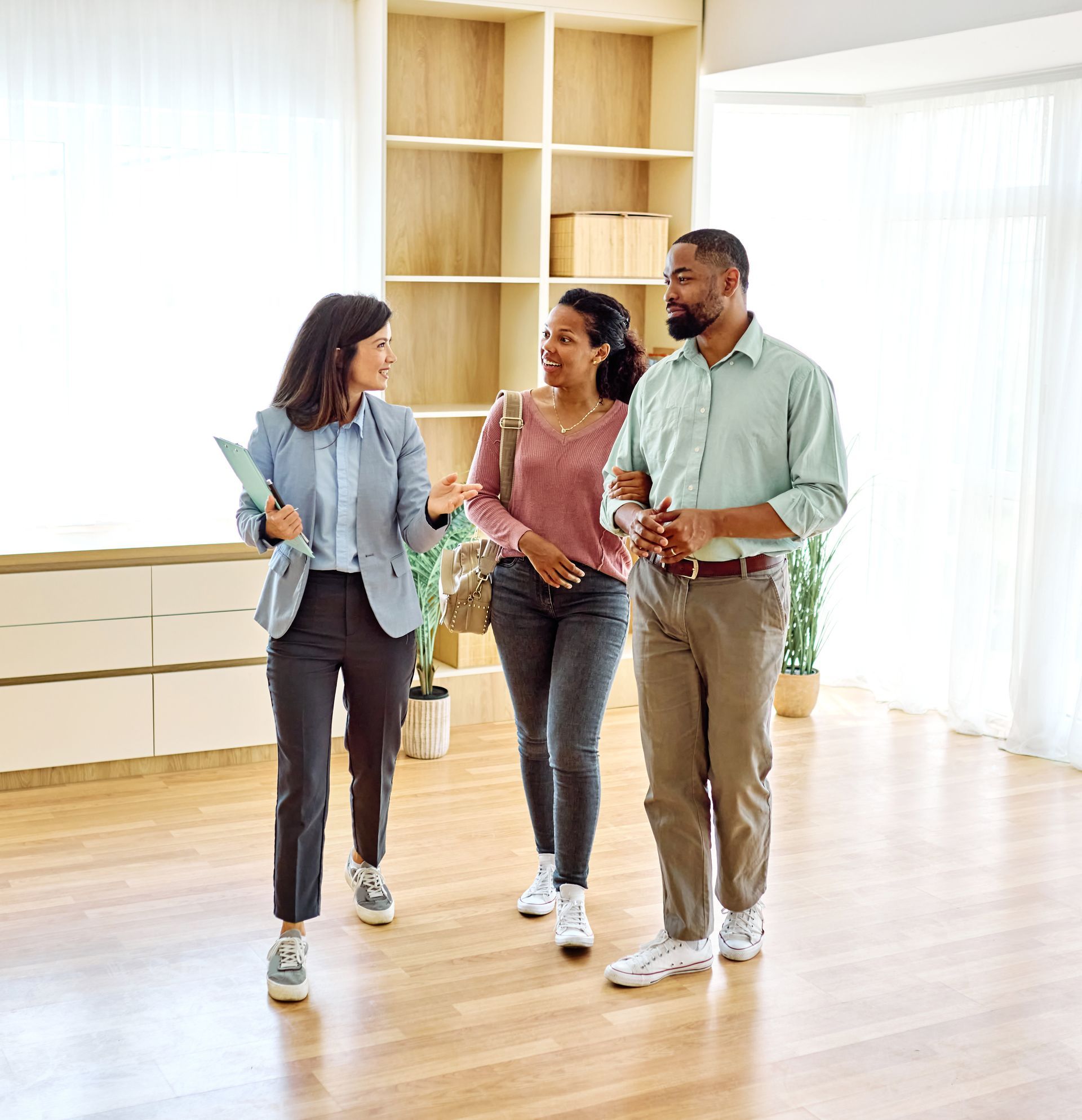 Three people talking in a bright, modern room with wood floors and large windows.