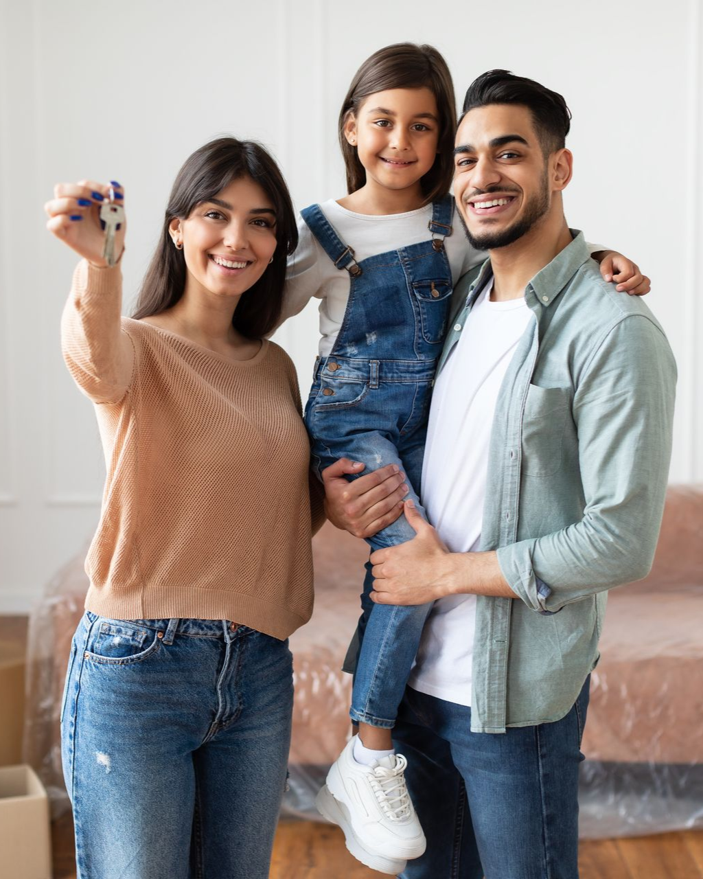 Smiling family of three posing indoors, with a child held between two adults in casual clothes.