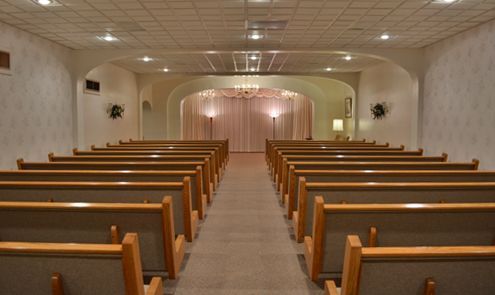 Empty chapel with wooden pews facing a softly lit altar.