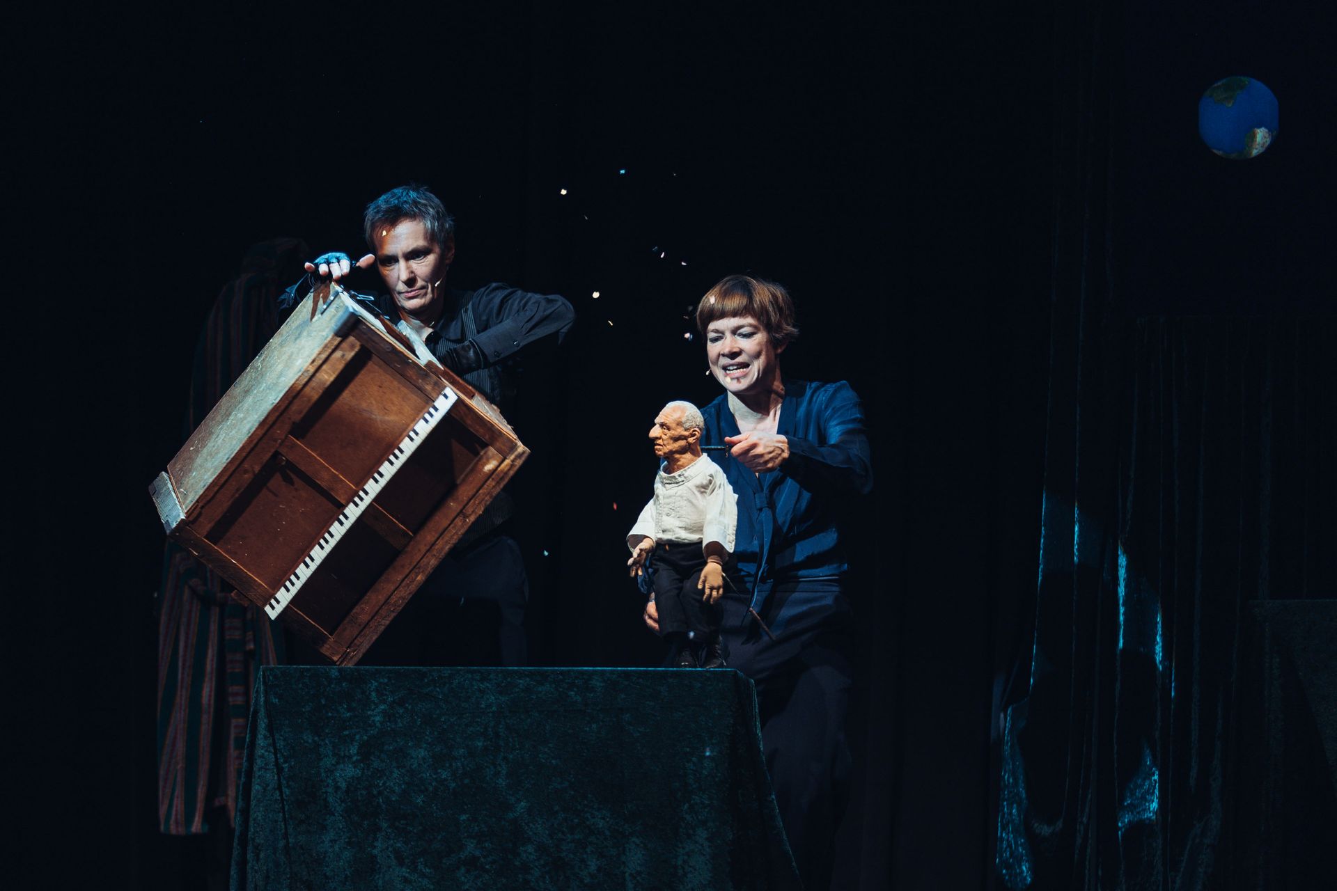 Zwei Personen auf einer Bühne mit einer Puppe und einem Klavier