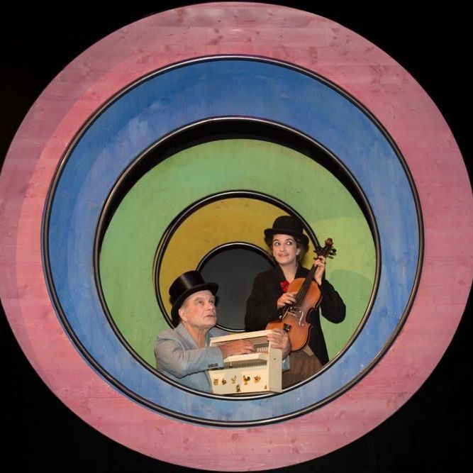 Ein Mann mit Zylinder spielt Geige, während eine Frau eine Schachtel hält