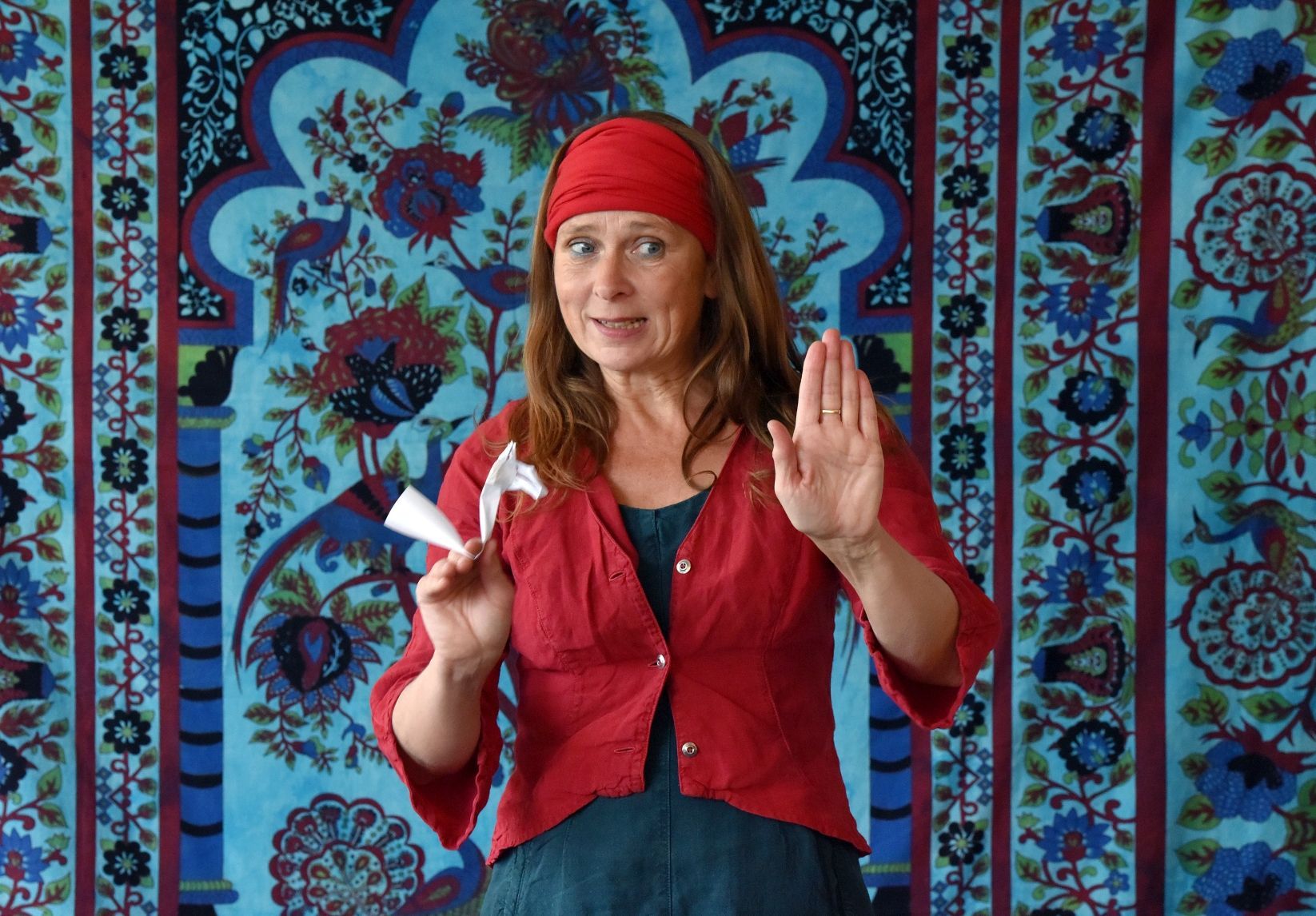 Eine Frau in einer roten Jacke steht vor einem bunten Wandteppich