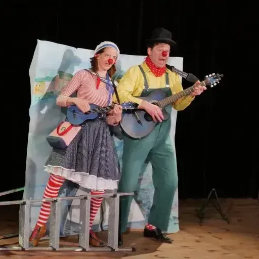 Ein Mann und eine Frau spielen auf einer Bühne Gitarre und singen in Mikrofone.