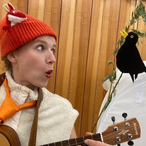 Eine Frau mit orangefarbenem Hut spielt Gitarre