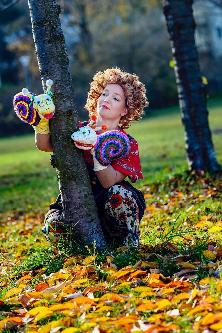 Eine Frau in einem Clownskostüm lehnt an einem Baum