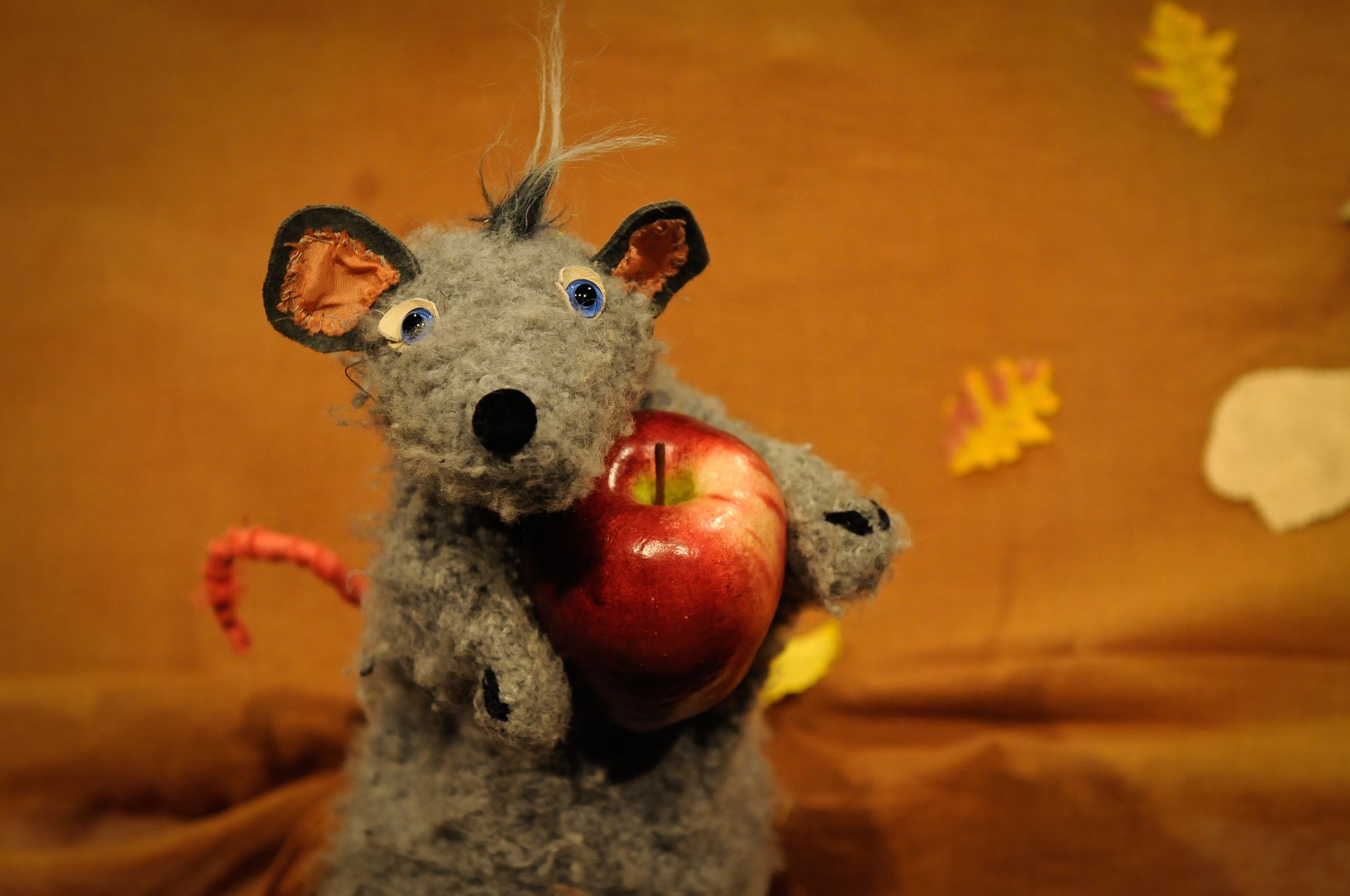 Eine ausgestopfte Maus hält einen Apfel in ihren Pfoten