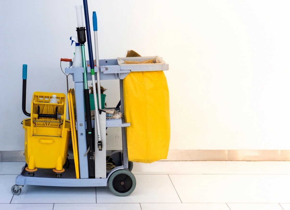 Cleaning cart with yellow buckets, mops, and a waste bag, against a white wall.