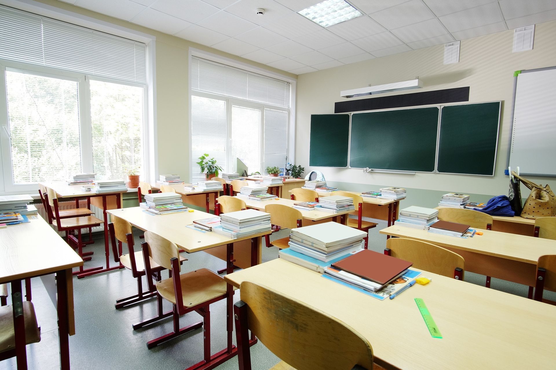 Empty classroom with desks, chalkboard, and windows.