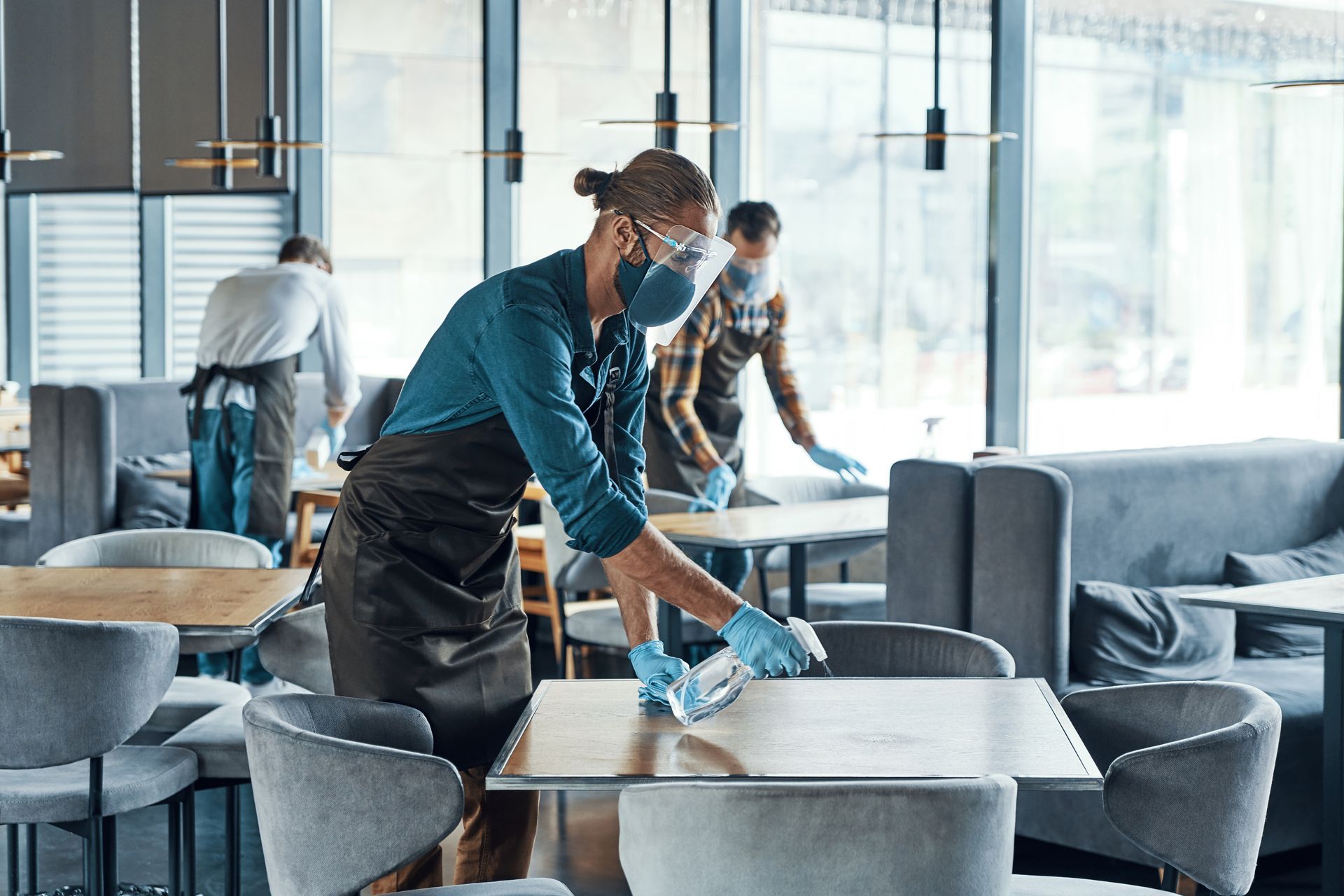 Restaurant staff sanitizing tables while wearing masks and gloves.