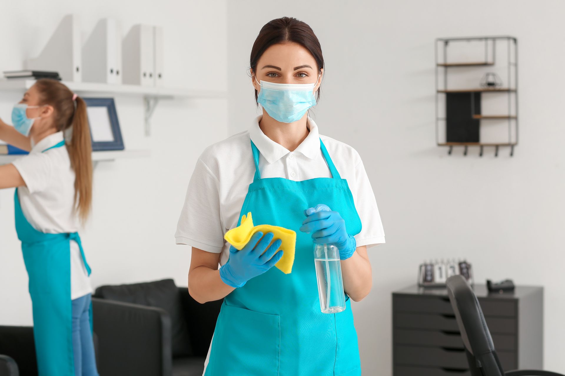 Two cleaning staff wearing aprons and masks, sanitizing an office. Two cleaning staff wearing aprons and masks, sanitizing an office.