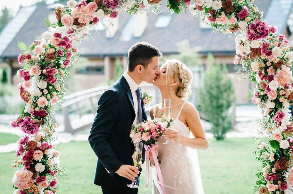 A Bride And Groom Are Kissing Under A Floral Arch At Their Wedding — Lynda Ross Marriage Celebrant In Alice River, QLD