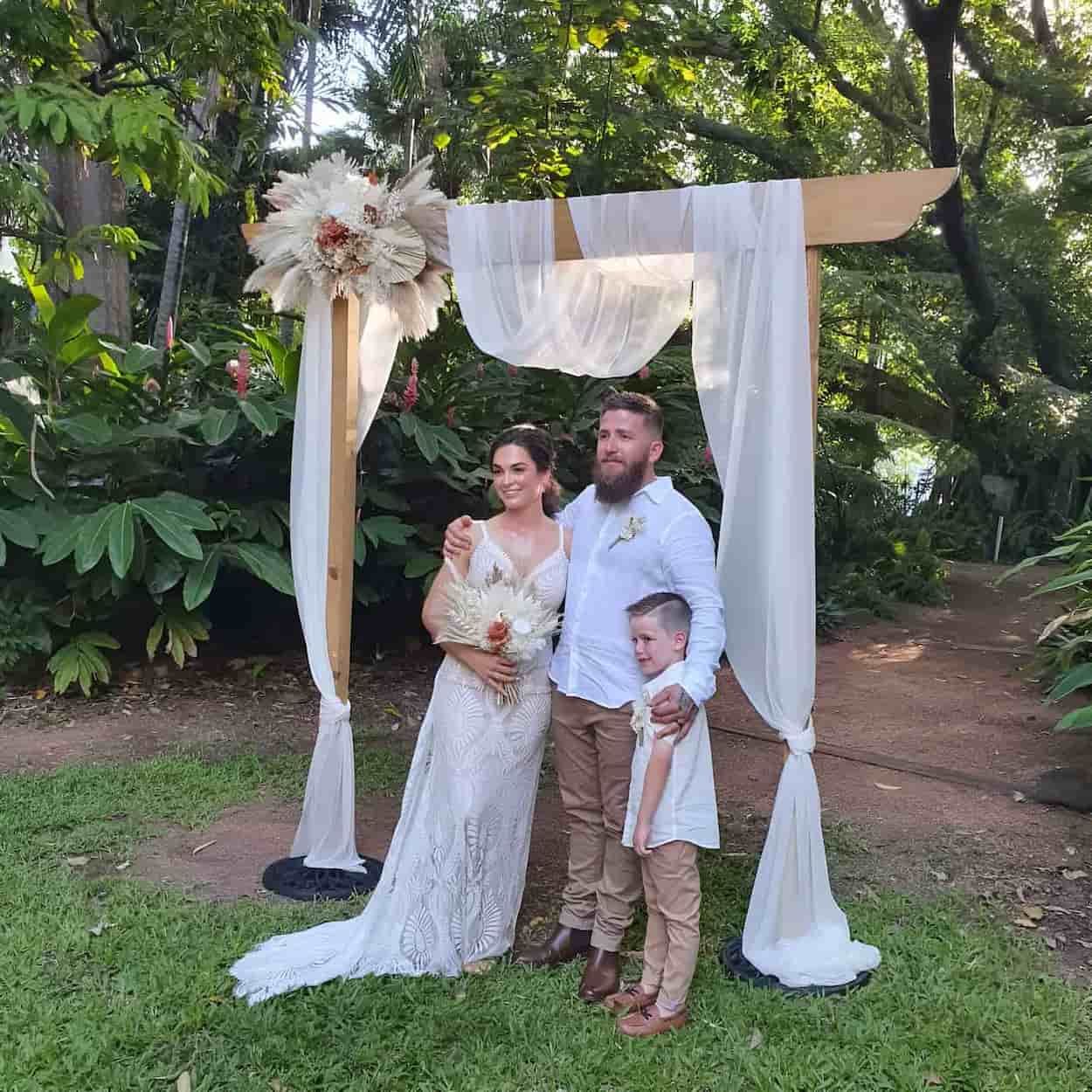A Bride And Groom Are Posing For A Picture With Their Son Under An Arch — Lynda Ross Marriage Celebrant In Alice River, QLD