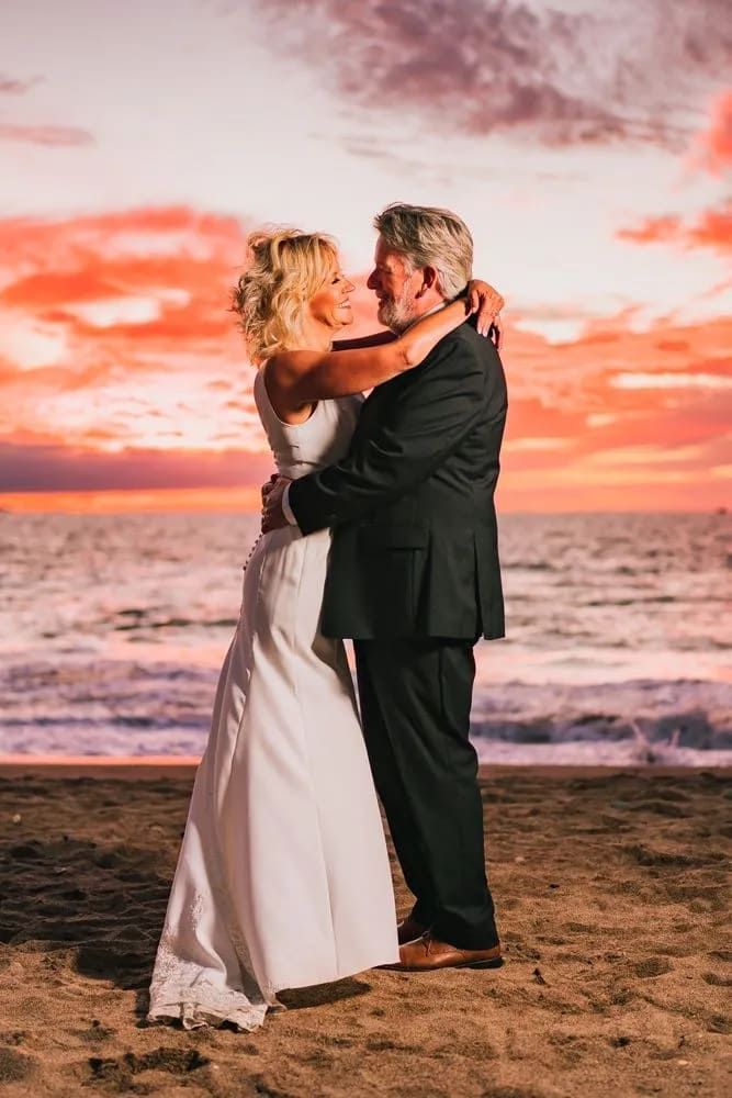 A Bride And Groom Are Hugging On The Beach At Sunset — Lynda Ross Marriage Celebrant In Magnetic Island, QLD