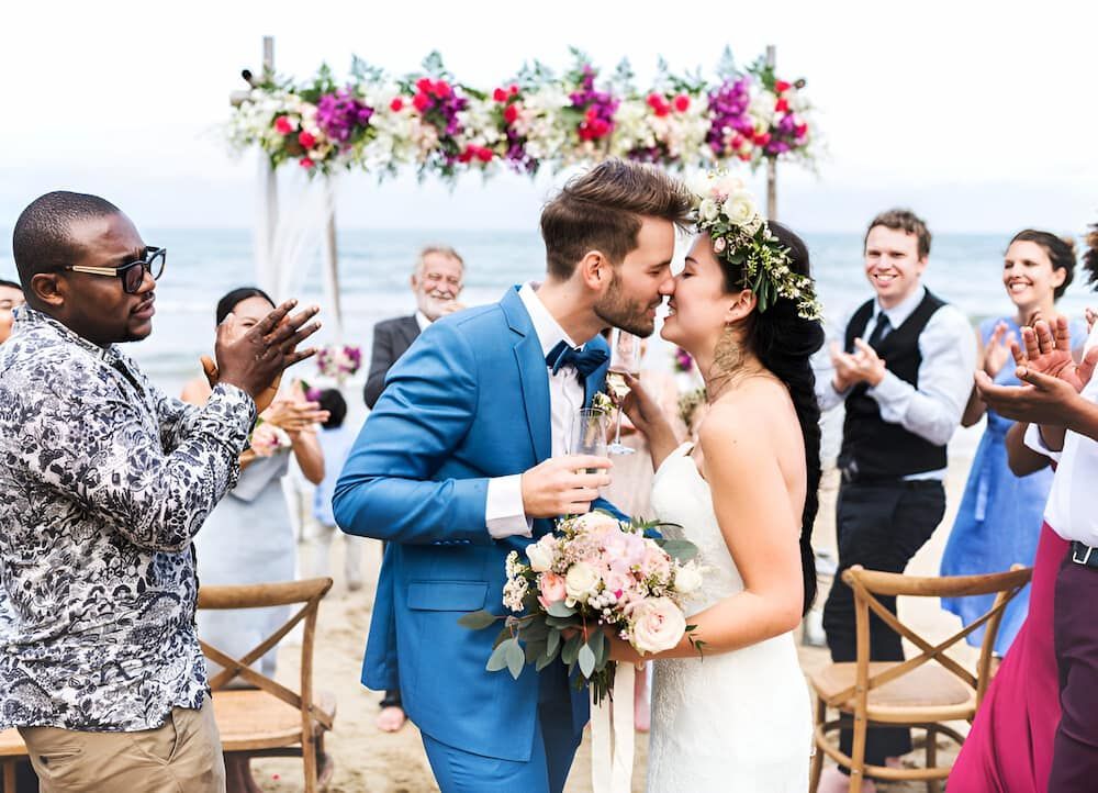 A Bride And Groom Pose For A Picture With People Celebrating in The Background — Lynda Ross Marriage Celebrant In Mission Beach, QLD
