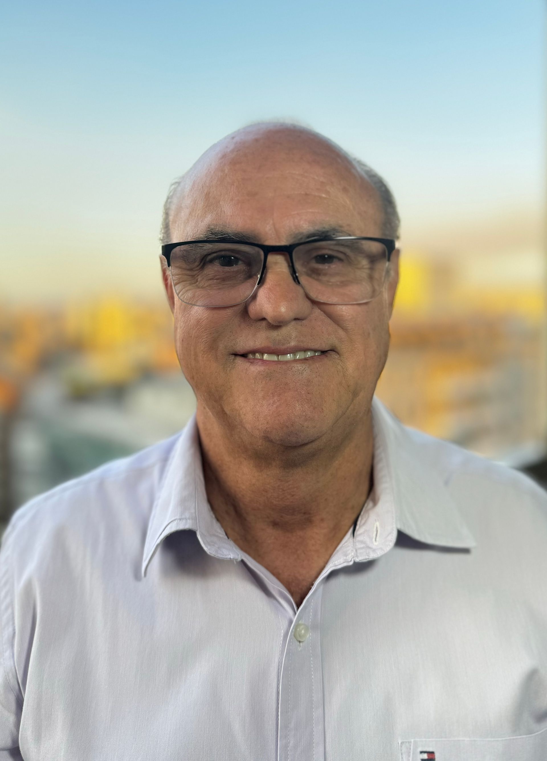 Um homem usando óculos e uma camisa branca está sorrindo para a câmera.