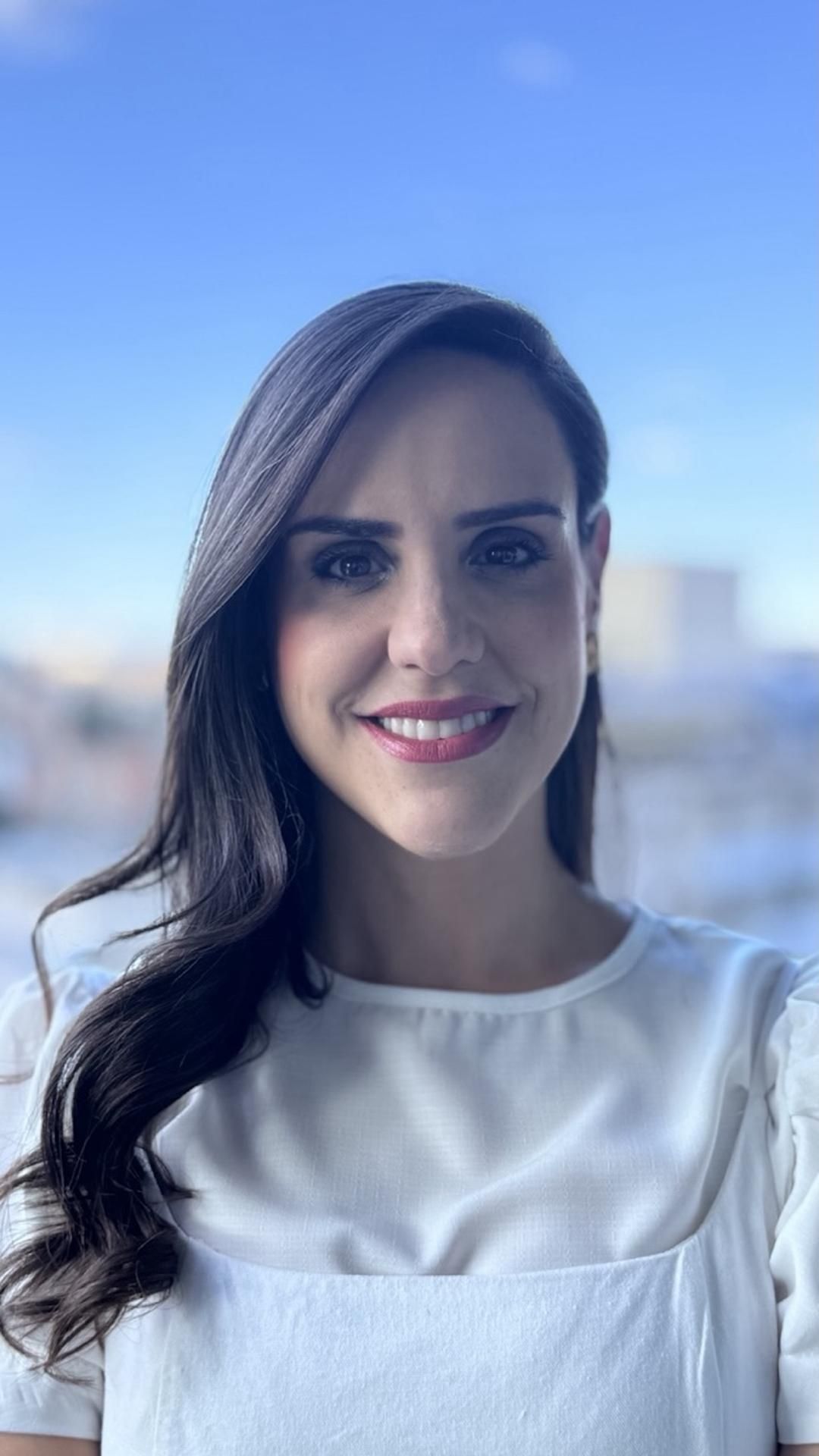 Uma mulher de camisa branca está sorrindo para a câmera.