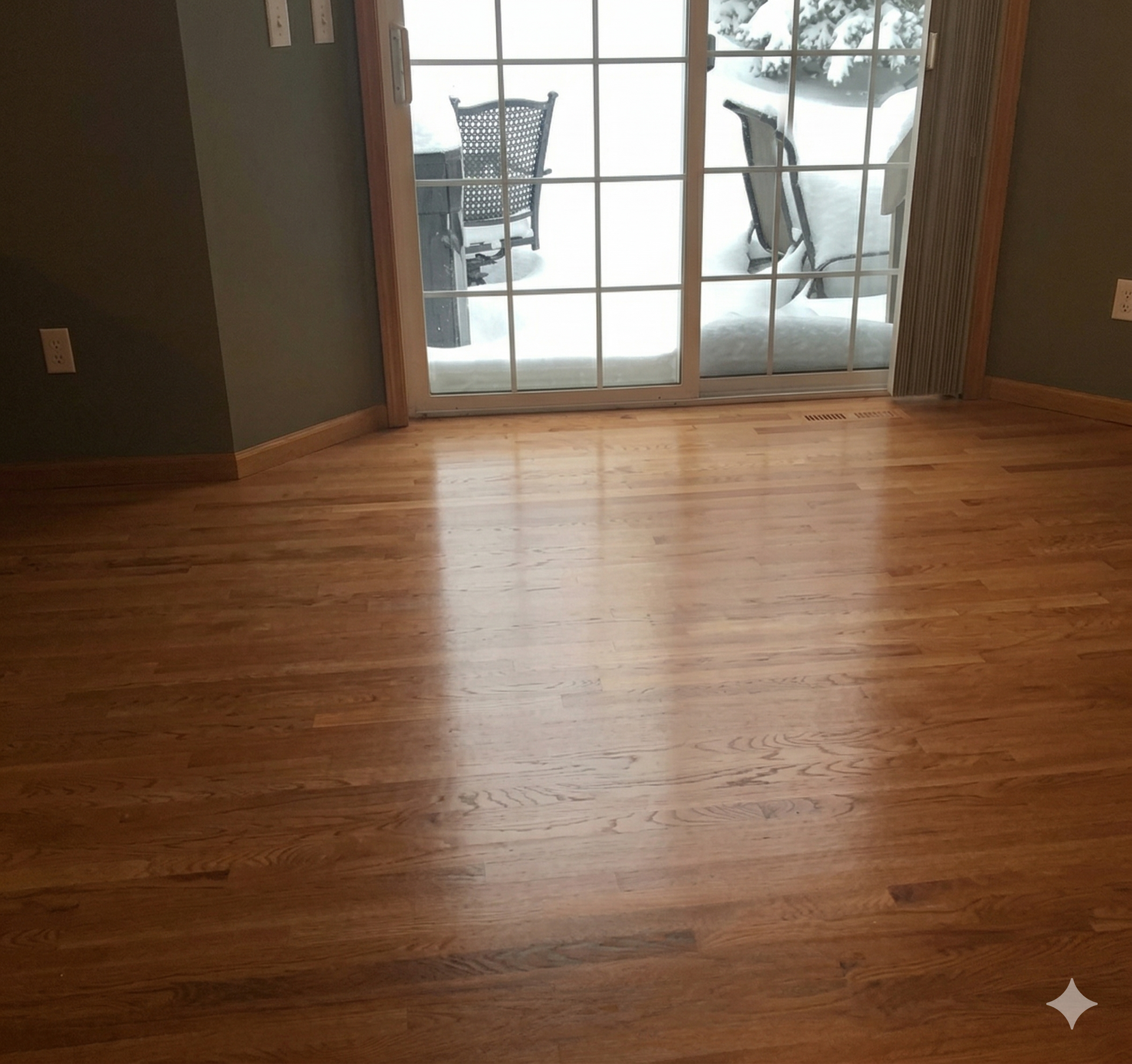 Polished hardwood floors lead to a sliding glass door revealing a snow-covered patio and chairs.