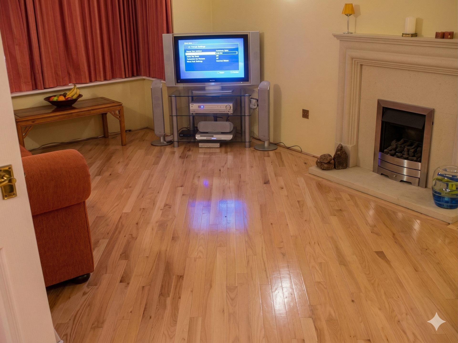 A living room with light hardwood floors, a television on a glass stand, a fireplace, and a couch in the foreground.