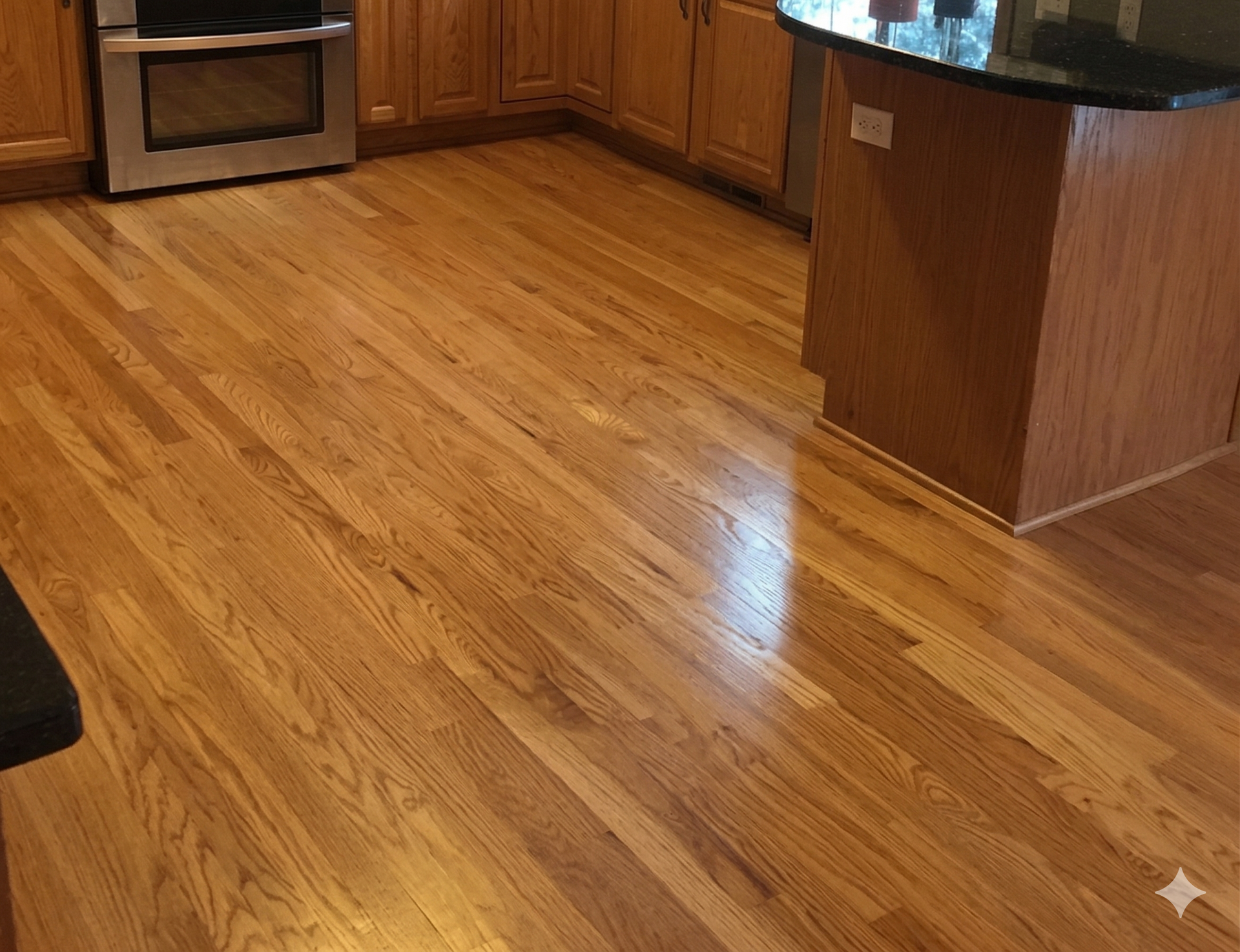 Kitchen with honey-toned hardwood flooring, light oak cabinets, a stainless steel oven, and a dark granite island.