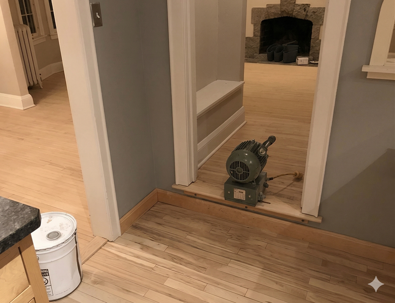 A green air mover fan sits on hardwood floors in a doorway between two rooms, one of which contains a stone fireplace.