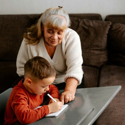 A woman is helping a young boy write in a notebook.