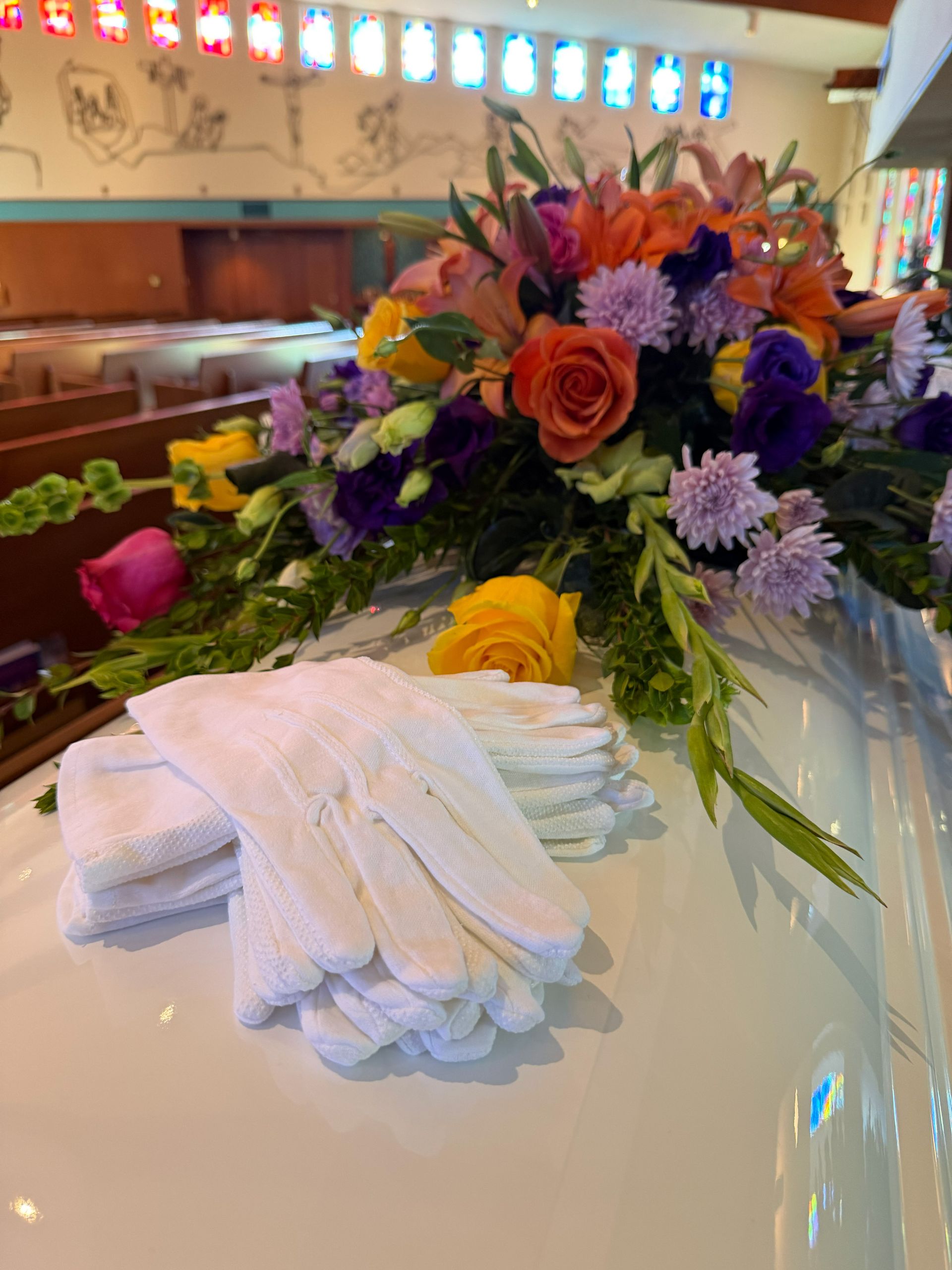 A closed brown casket adorned with flowers, candles, and sheer fabric against a green wall.