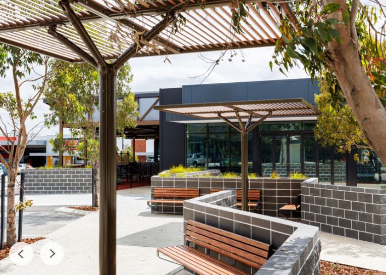 A park with benches and umbrellas in front of a building.
