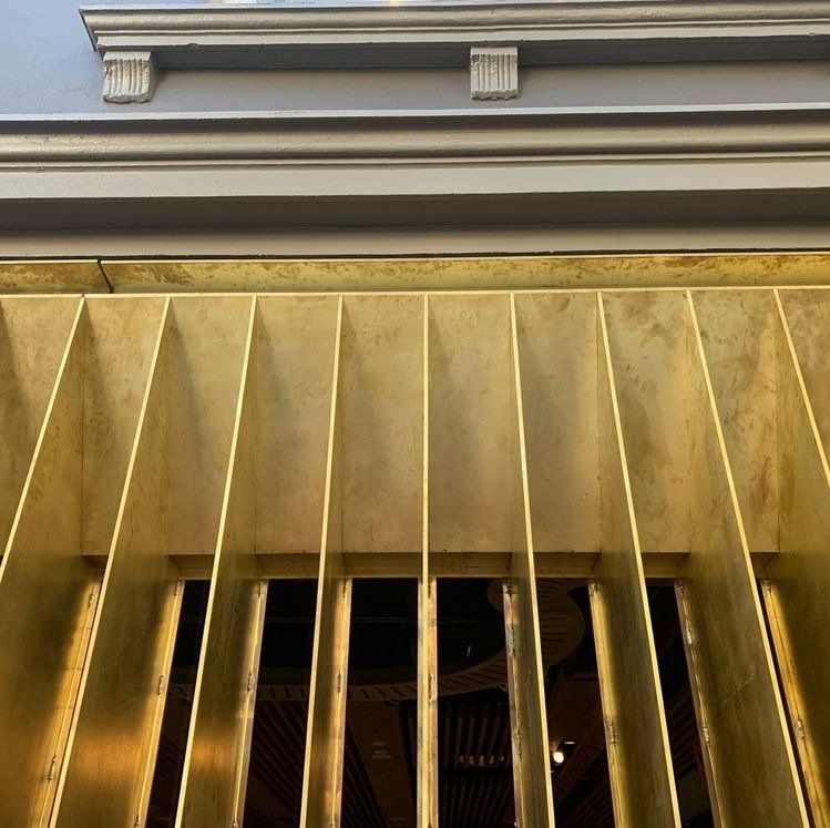 Gold metal grill with vertical bars beneath a building cornice and decorative molding