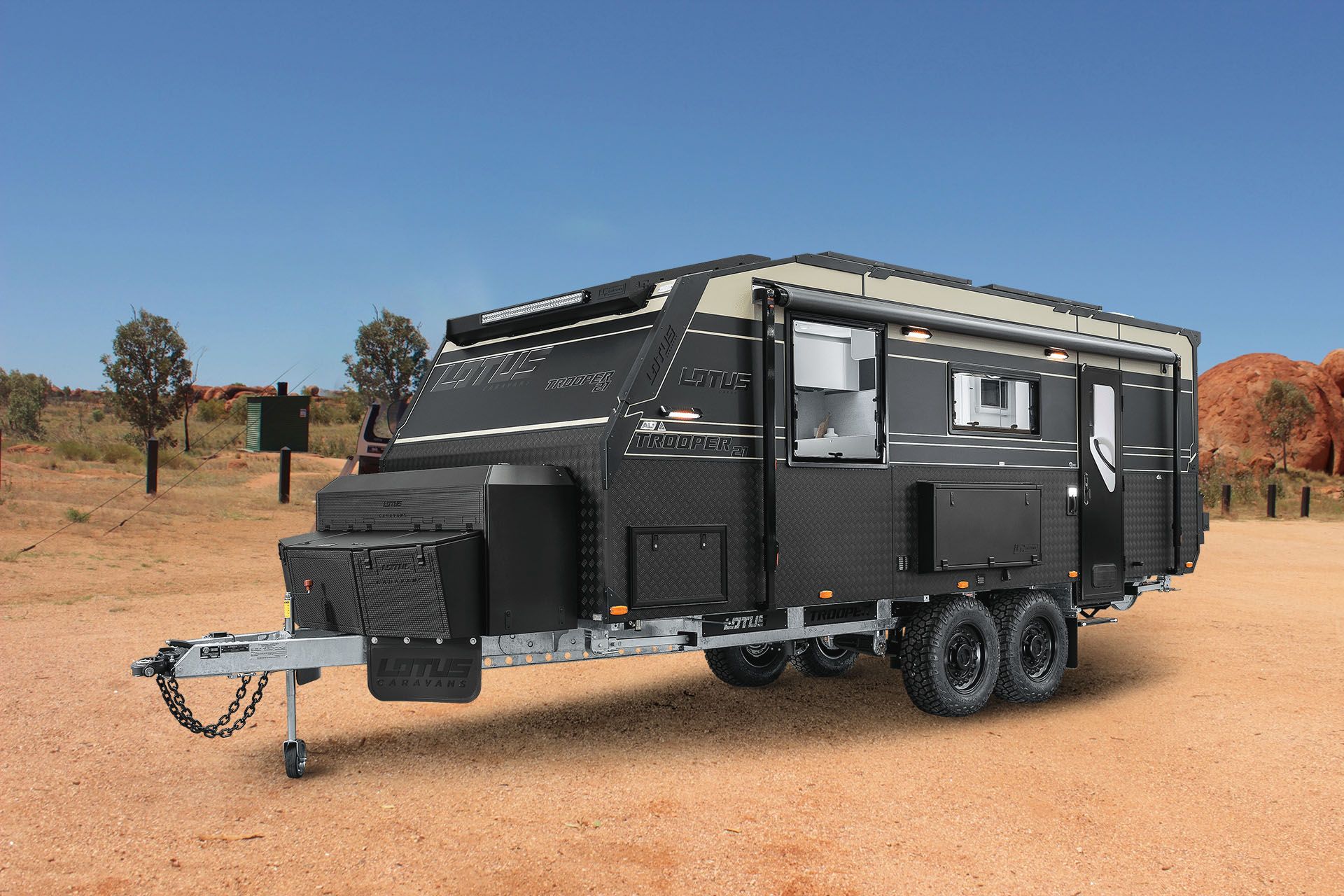 Black off-road travel trailer parked on a dirt road in a desert landscape