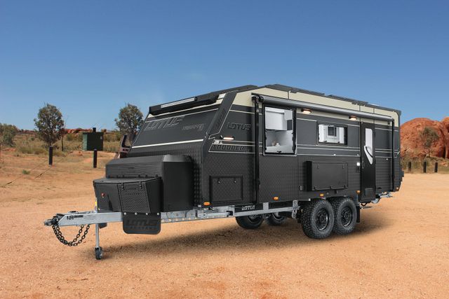 Black off-road travel trailer parked on a dirt road in a desert landscape